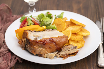 roasted piglet with potato chips and orange on white plate