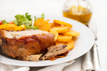 roasted piglet with potato chips and orange on white plate