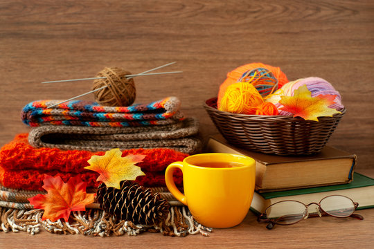 Knitting and autumn. Yarn, a cup of tea, knitting needles, glasses, books for knitting in a cozy atmosphere. Maple leaves and spruce cones are reminiscent of autumn. Knitting warm clothes.