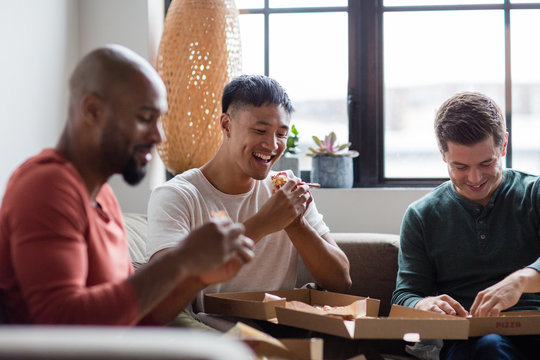 Male friends eating takeout pizza in an apartment