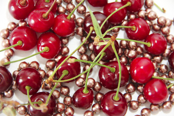  red cherry with green leaves and pink beads on a white background
