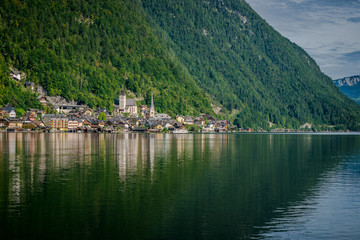 Travel to the Alps. City Hallstatt. City among the mountains in the Alps. Hallstatt is beautiful small town in Austria. town is reflected in the water on a sunny day
