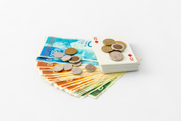 A deck  of playing cards with coins lies on a stack of banknotes and coins of new Israeli shekels -...