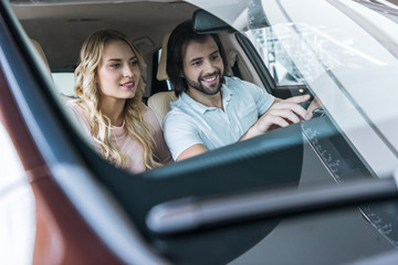 young couple sitting in car at dealership salon