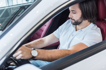 bearded man sitting in new car for test drive in dealership salon