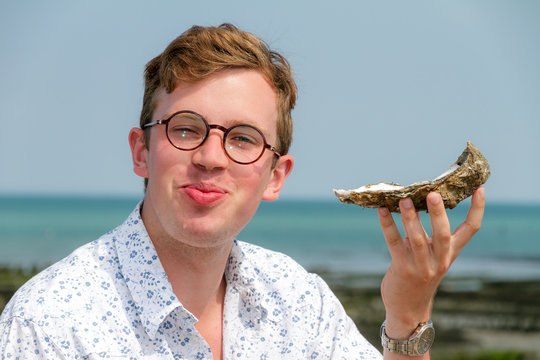 Young man enjoys the taste of a rare big oyster called a pied de cheval (horse's hoof) at the french coast of Brittany (Bretagne) in Cancale, France on a summer day
