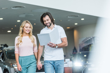 young couple with catalog buying car at dealership salon
