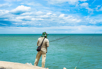 The man standing fishing the seaside and the blue sky.