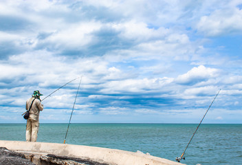 The man standing fishing the seaside and the blue sky.