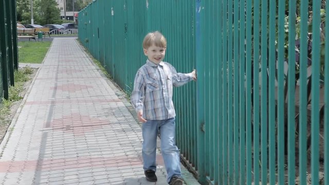 Little boy walks along the iron fence