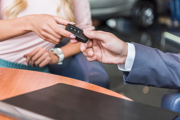 Obraz na płótnie Canvas cropped shot of dealership salon seller giving car key to woman in auto salon