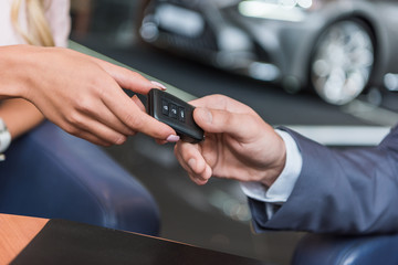 partial view of dealership salon seller giving car key to woman in auto salon