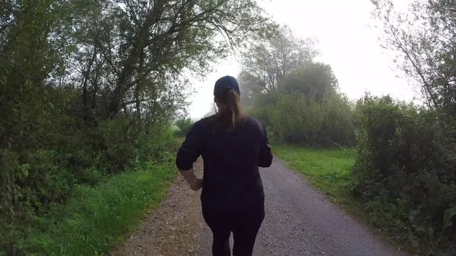 Behind a female runner running on a gravel road on a foggy morning