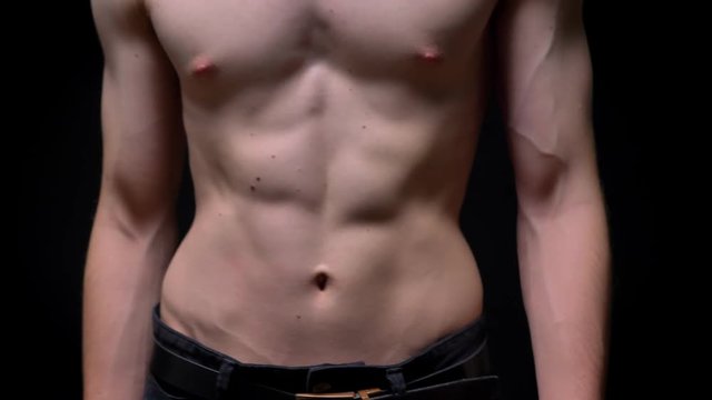 sporty topless caucasian man walking in camera and demonstrating his fit body on dark background in studio