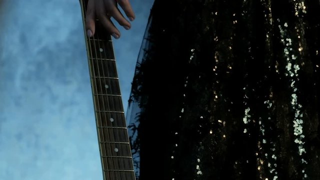 Guitar fretboard in the foreground. The girl in the concert dress comes up and gently passes her hand over the strings. Theme for the musical day.