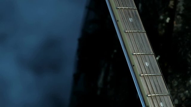 Guitar fretboard in the foreground. Close-up of female fingers. The girl in the concert dress comes up and gently passes her hand over the strings. Smoky background. Theme for the musical day.