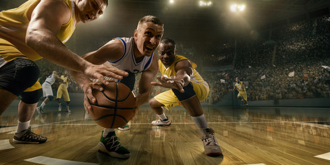 Basketball players on big professional arena during the game. Tense moment of the game. Male caucasian and black players fight for the ball © Alex