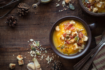 Traditional Thanksgiving homemade pumpkin or squash soup garnished with bacon, croutons and seeds. Overhead view
