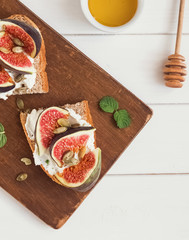 Toasts with ricotta cheese, figs and honey on the wooden board, top view.