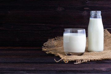 A bottle and a glass of milk on wooden background.