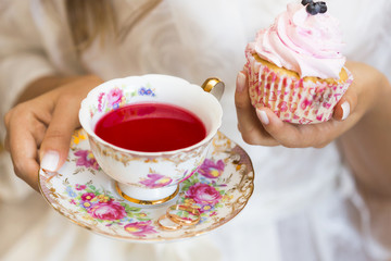 Капкейк, пирожное с кремом и чашка с чаем в руках девушки 