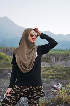 Portrait of Hijab Muslim Girl wearing a camouflage soldier pants over a blur mountain background.