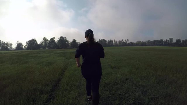 Tracking shot of a woman running on the field in the morning