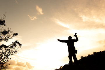 Fototapeta na wymiar Silhouette of man hold up hands on the peak of mountain,success concept