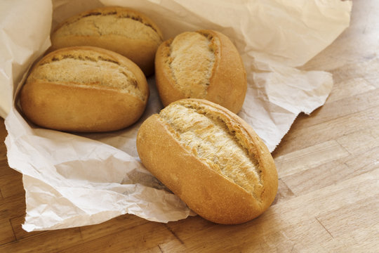 bread rolls or buns for breakfast fresh from the bakery in a white paper bag on a wooden table