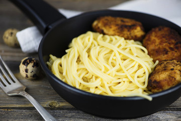 Spaghetti with meat cutlets in a frying pan on a wooden board