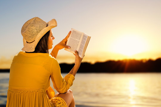 Woman reading a novel on beach at sunset.