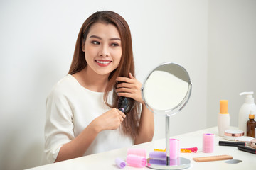 Getting rid of tangles. Beautiful young woman looking at her reflection in mirrorand brushing her long hair while sitting at the dressing table