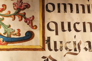 A close up view of an old book sheet made of parchment with some blackletter Latin writings and a colored miniature