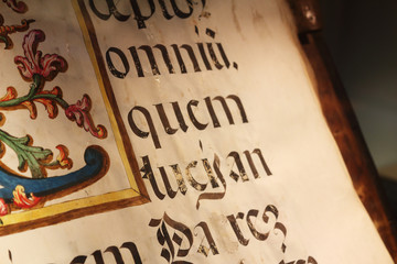 A close up view of an old book sheet made of parchment with some blackletter Latin writings and a colored miniature