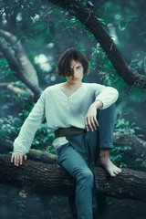 Portrait of handsome man with crown in forest sitting on branch of the tree at night. Prince of...