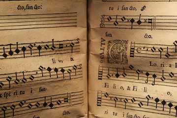 An old score written on a parchment, showing a few staves with notes and a miniature, for a song in Latin