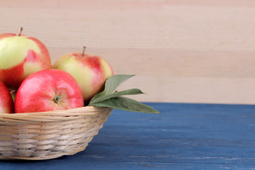 Fresh ripe red apples with leaves in a basket on a blue wooden table and on a background of natural wood with a place for an inscription
