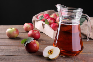 apple juice in a jug next to fresh red apples on a brown wooden table