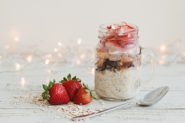 Horizontal photo of overnight oats with strawberry and milk served on wooden table with spoon, fresh berries and lights for home decor
