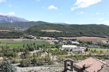 A landscape of the Pyrenees mountains with green forests and a blue sky with some clouds in the...