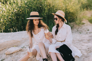 attractive girlfriends in straw hats with cups of coffee latte sitting on ground