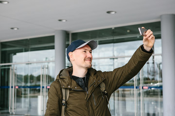 A guy in a baseball cap or a tourist photographs or does selfie on the phone and smiles.