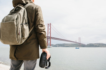 The man holds the virtual reality glasses and looks at the 25th of April bridge in Lisbon. The...