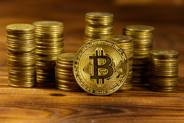 Golden bitcoin and stacks of coins on wooden background
