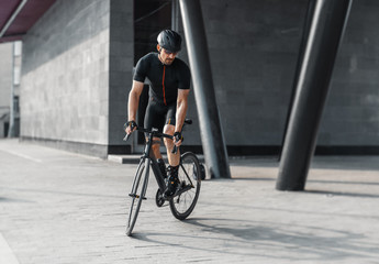 Sportsman riding bike next to modern building inside urban bridge.