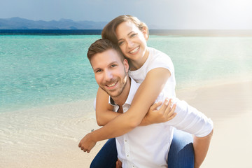 Happy Man Giving Piggyback To His Wife At Beach