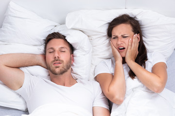 Woman Covering Her Ears While Man Snoring On Bed