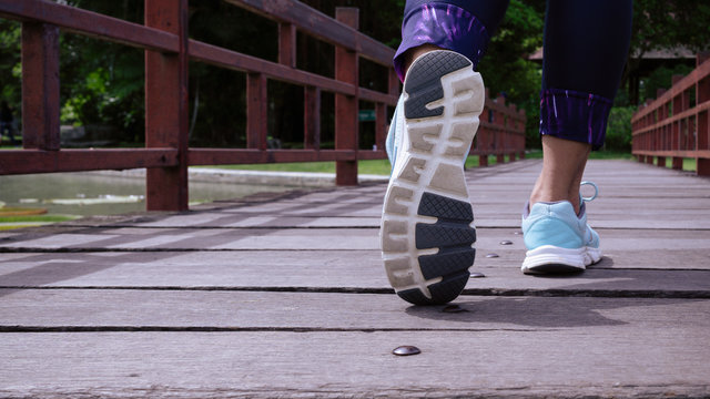 Sporty women walking on the wooden bridge, Close up of feamale sport shoes walking or jogging alone at park in the morning, Sports healthy lifestyle concept.