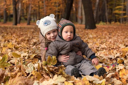 Dzieci zasypane w liściach jesienią w parku. Rodzeństwo.