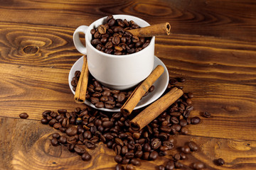 Coffee beans in white cup and cinnamon sticks on wooden table
